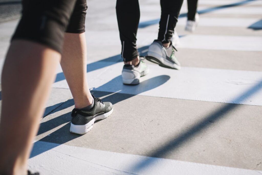 People walking across a crosswalk in athletic shoes, symbolising reaching 10,000 steps a day for better health and fitness – Me Muscle Nutrition.